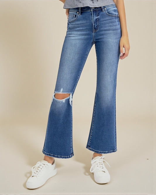 Person wearing blue flared jeans with a ripped knee on a beige background