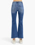 Rear view of a person wearing blue flare jeans and white sneakers against a plain light gray studio background.