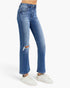 A model wearing a pair of high-waisted, straight-leg blue jeans with a distressed rip on the left knee, paired with white sneakers against a light gray studio background.