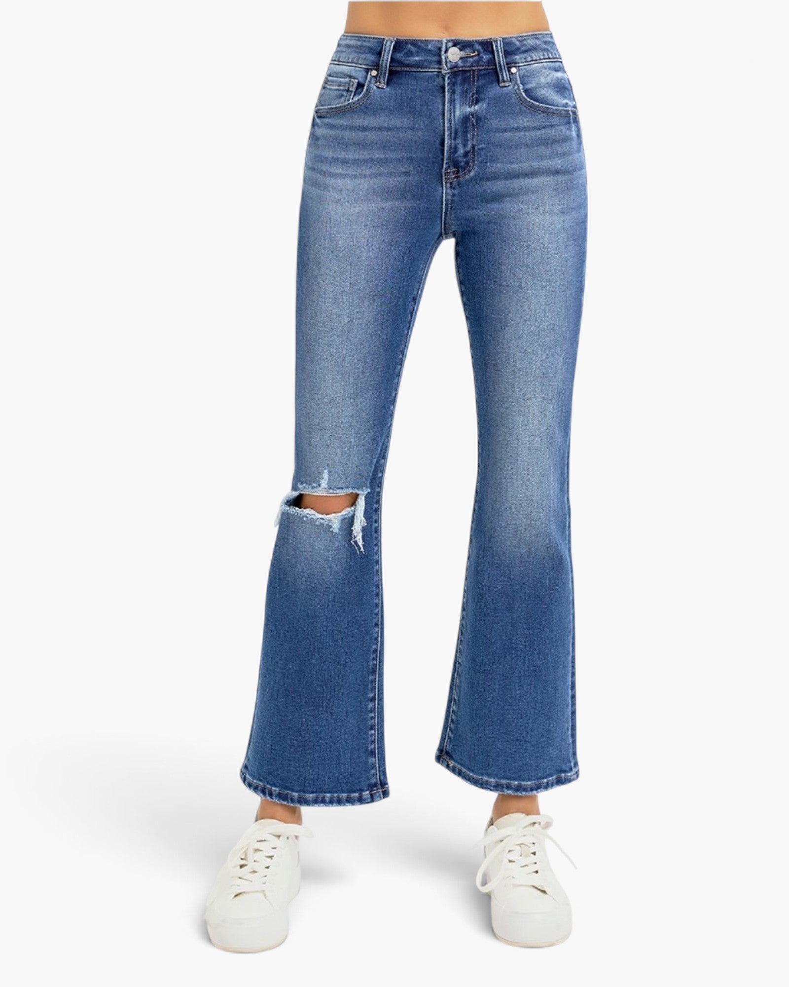 A person wearing medium-wash blue denim flare jeans with a distressed rip at the knees and white sneakers, shown against a plain light gray studio background.