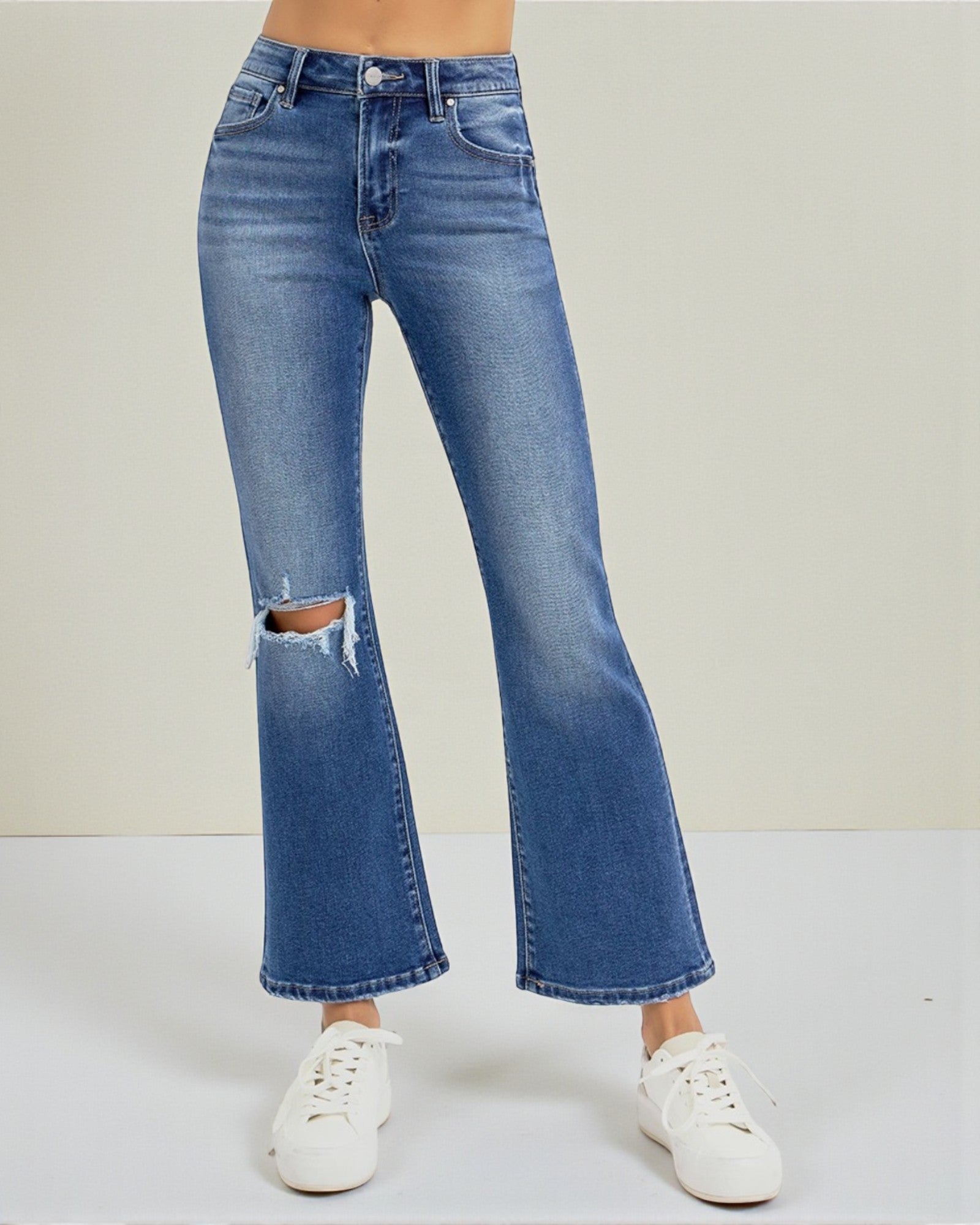 Blue flared jeans with a ripped knee on a white background