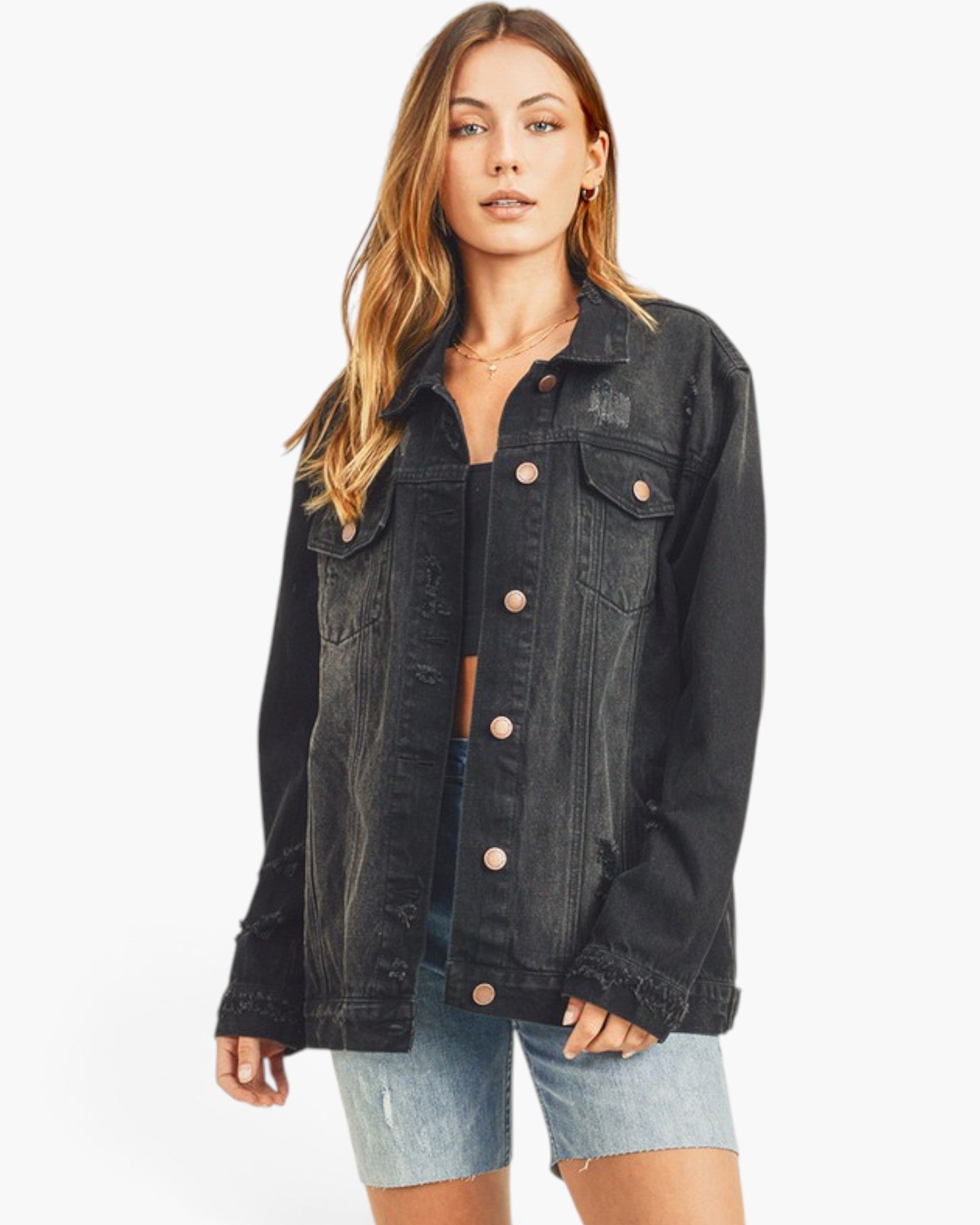 A woman modeling a black washed denim jacket with rose gold buttons, paired with light blue denim shorts, against a plain white background.