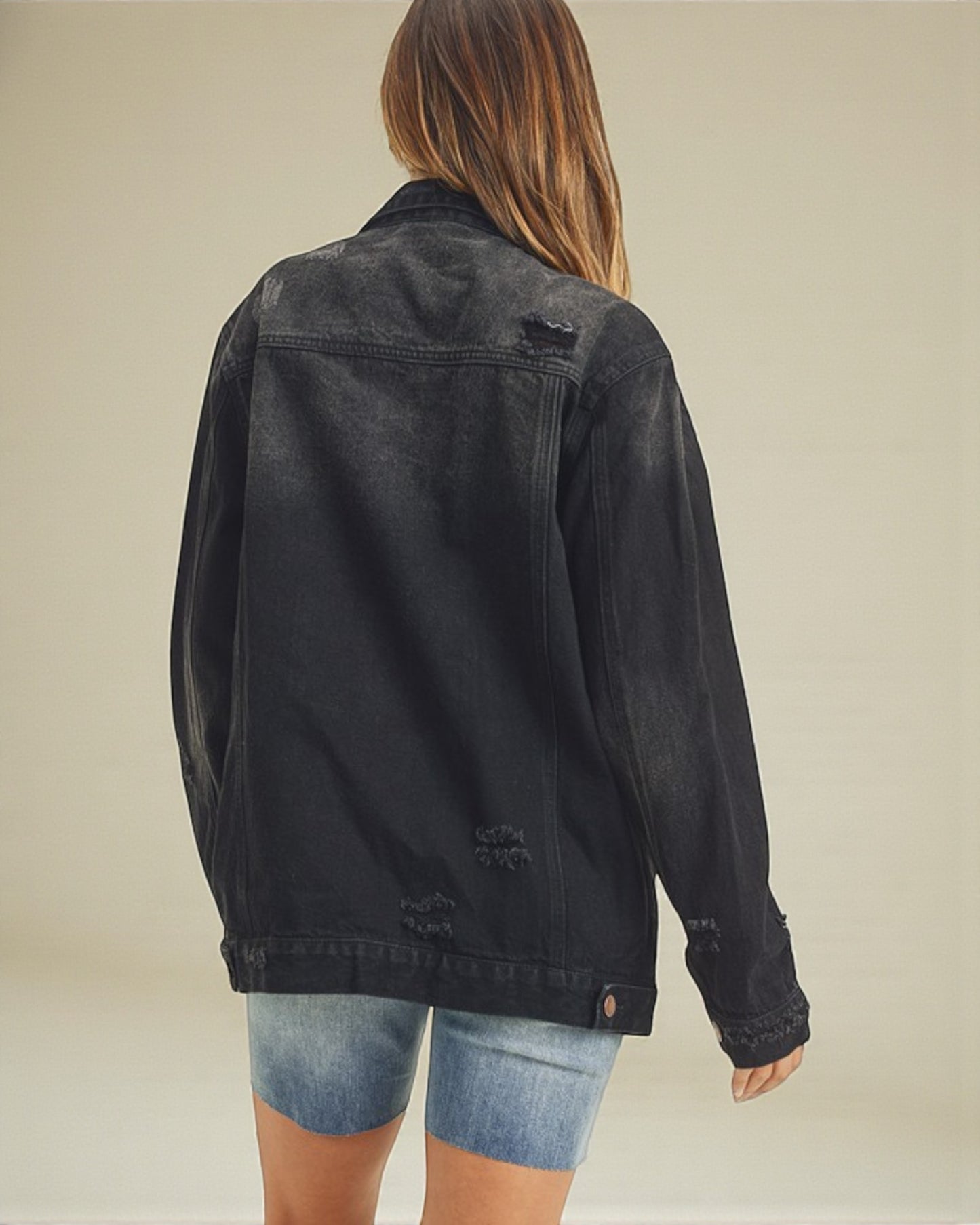 Person wearing a black denim jacket on a beige background