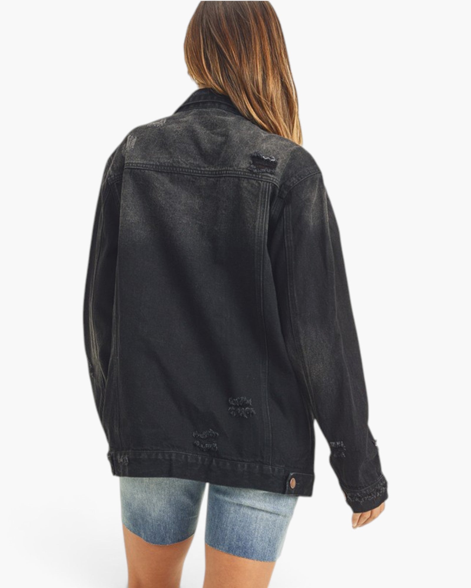 A woman shown from the back wearing a faded black denim jacket with distressed details and light blue denim shorts against a plain white background.