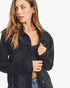 A woman wearing a black distressed denim jacket over a black top and blue jeans, photographed against a clean white background.