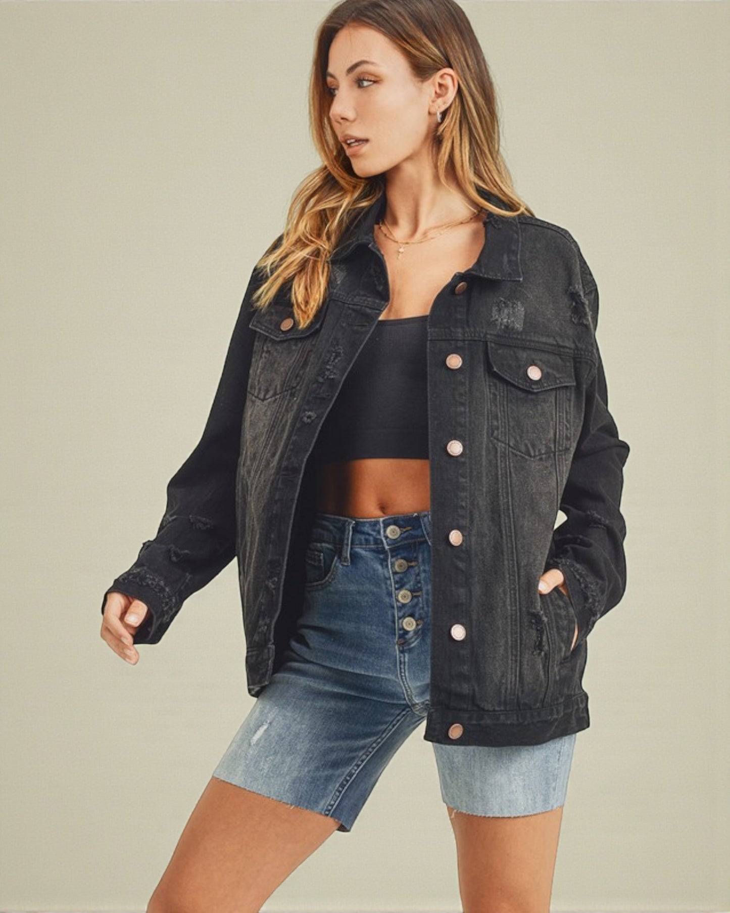 Woman wearing a black denim jacket and blue shorts on a beige background