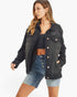 A woman modeling a black distressed denim jacket over a black crop top and light-wash denim shorts against a plain white background.