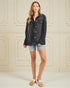 Woman wearing a black denim jacket and light blue shorts against a white paneled wall.