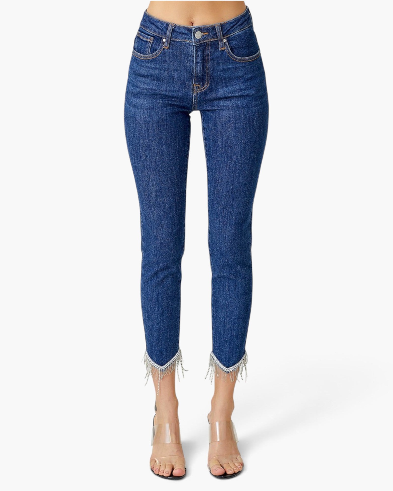 A model is wearing a pair of high-waisted, cropped blue denim jeans with frayed hems, paired with clear high-heeled sandals, shown against a plain white studio background.