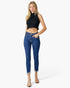 A woman modeling a black sleeveless crop top and blue high-waisted ankle-length jeans with frayed hems, paired with nude high heels, against a plain white studio background.