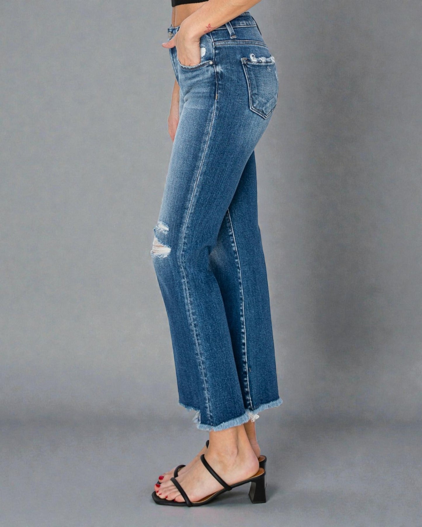 Blue jeans with distressed details worn by a person on a gray background