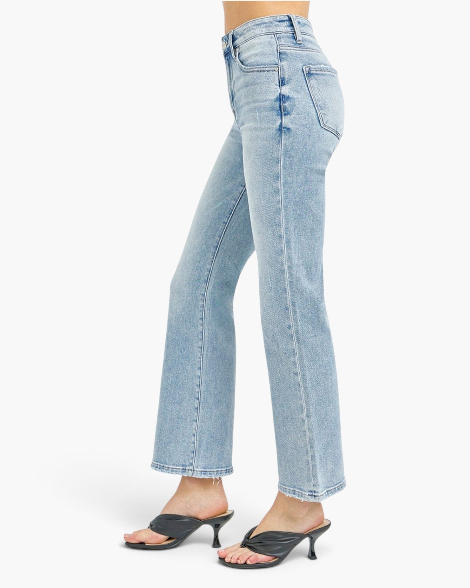 Light wash blue denim jeans shown on a model from the waist down, paired with black heeled mule sandals against a plain white studio background.