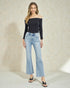 Woman wearing a black off-shoulder top and light blue jeans against a neutral background