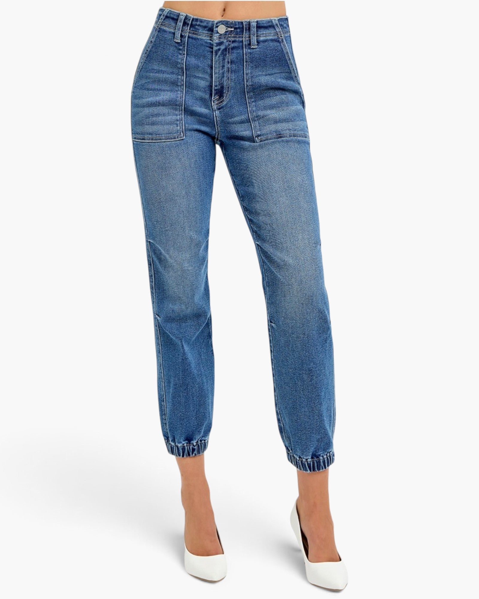 A model wearing medium wash blue denim cropped pants with a straight-leg fit, elastic cuffs, and front patch pockets, paired with white pointed-toe heels against a light gray studio background.
