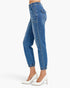 A side profile view of a person wearing blue high-waisted cropped jeans with elastic cuffs, paired with white pointed-toe heels, against a plain light gray background.