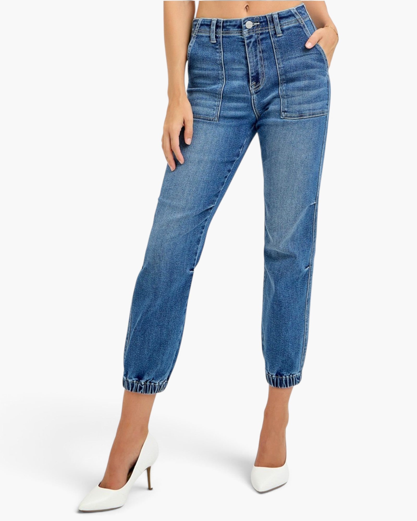 A model wearing medium wash blue cropped jeans with a straight-to-slightly-relaxed leg, cuffed hems, and front patch pockets, paired with white pointed-toe heels against a light gray studio background.