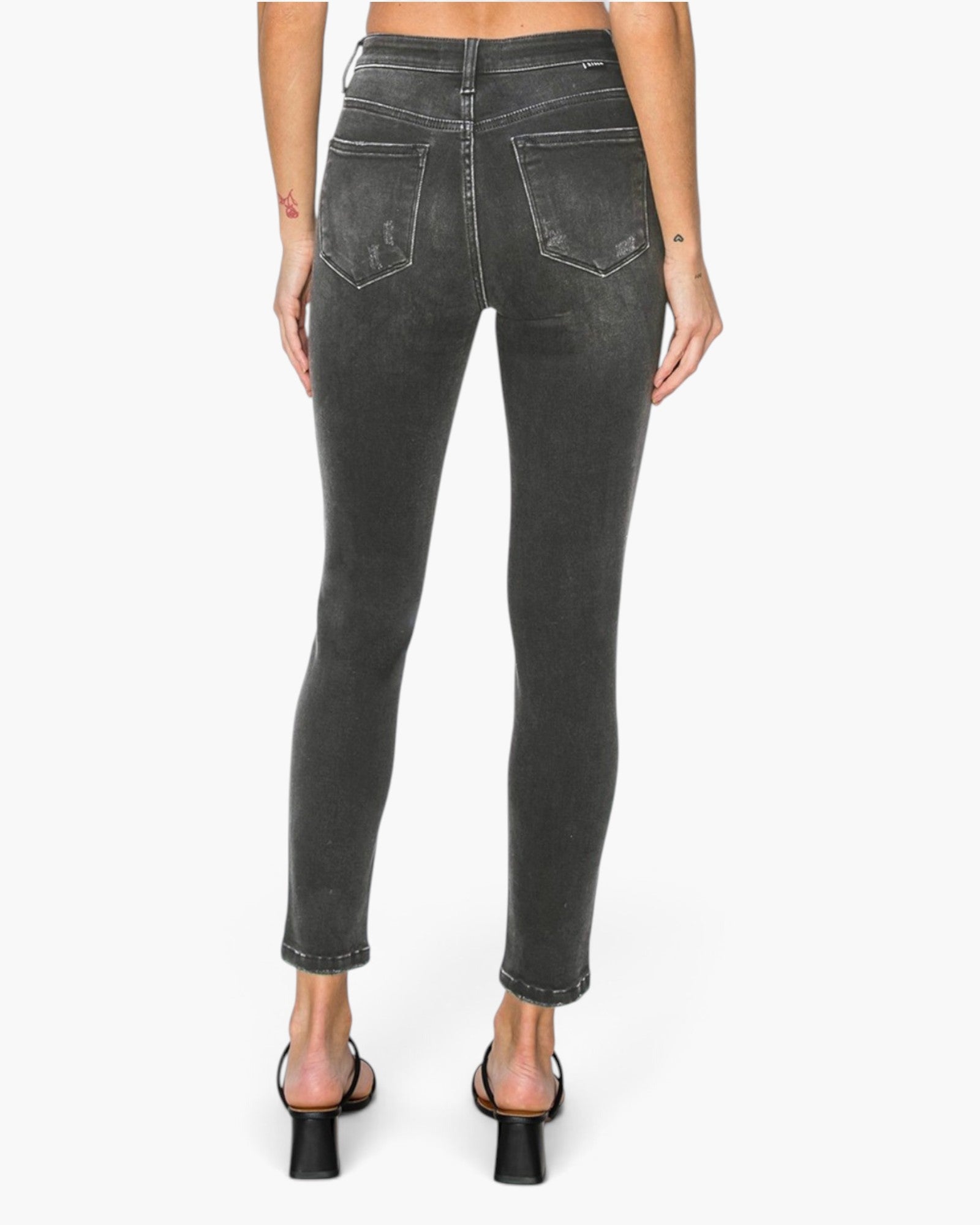 Rear view of a model wearing dark gray washed skinny jeans with rolled cuffs and black block-heel sandals against a plain white background.