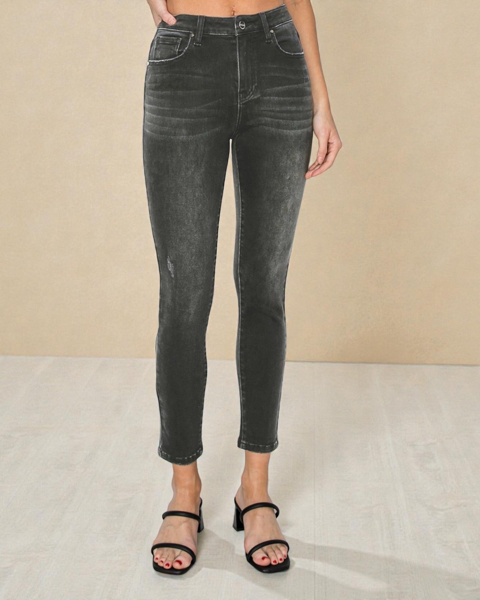 Person wearing black acid-wash jeans on a beige background