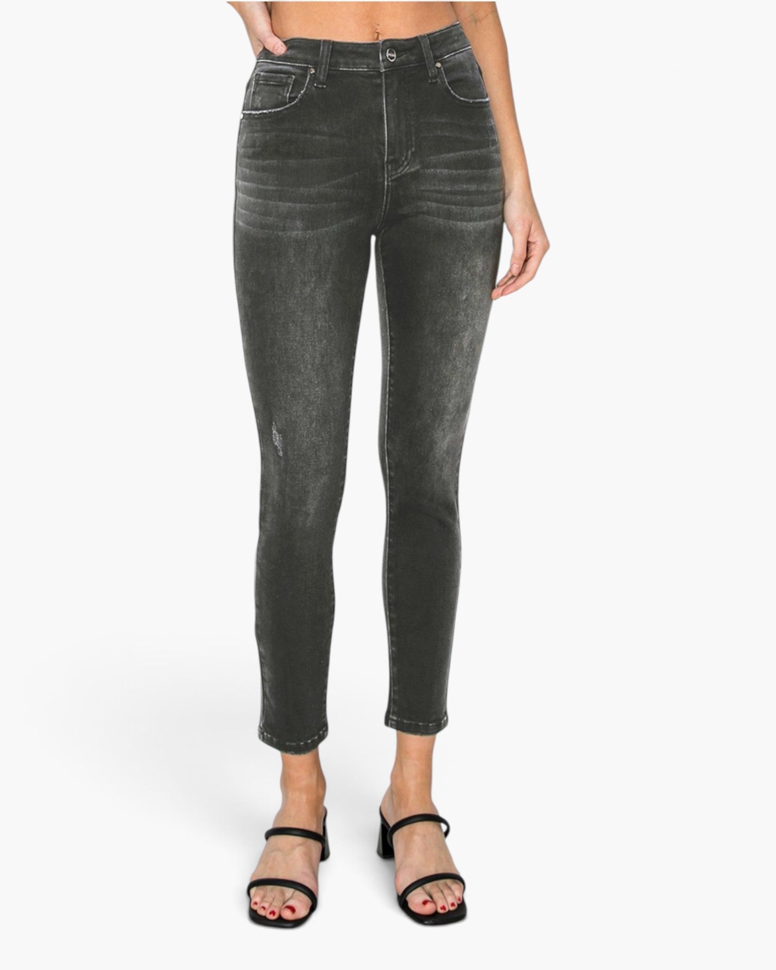 A model wearing a pair of dark gray washed skinny jeans with a distressed, faded finish, paired with black strappy sandals against a plain white studio background.