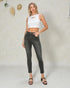 Woman wearing a white crop top and black jeans against a plain background