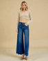 Woman wearing a beige cropped sweater and blue jeans against a beige background