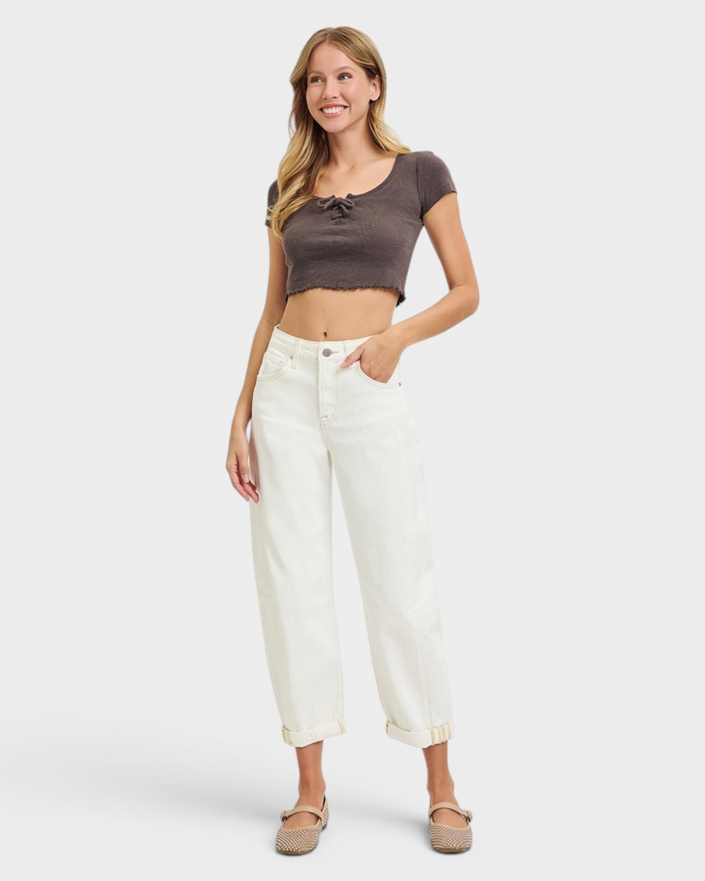 Woman wearing a brown crop top and white pants on a white background