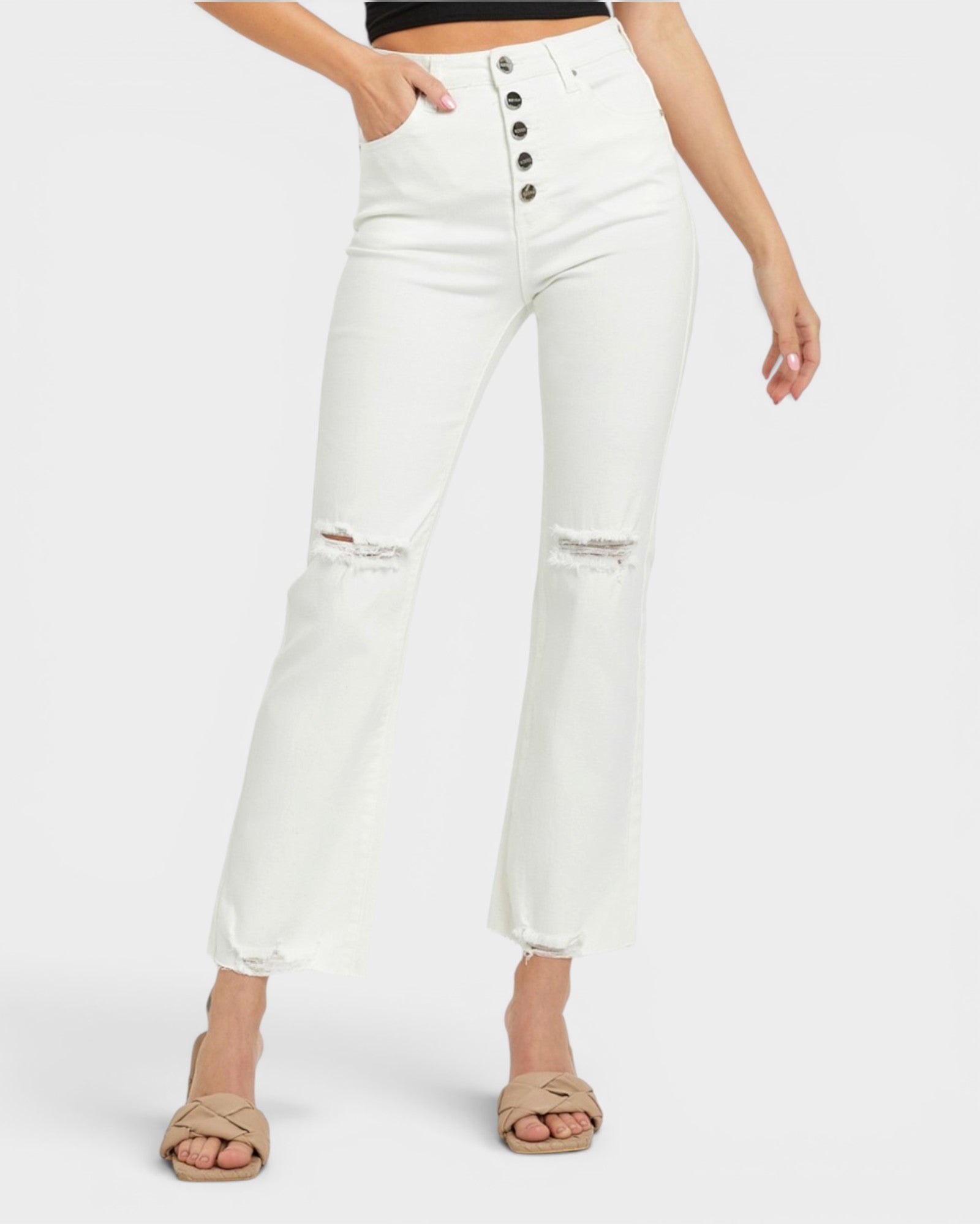 White cropped jeans with a high waist, button fly, and distressed knee details, shown on a model wearing beige heeled sandals against a light gray background.
