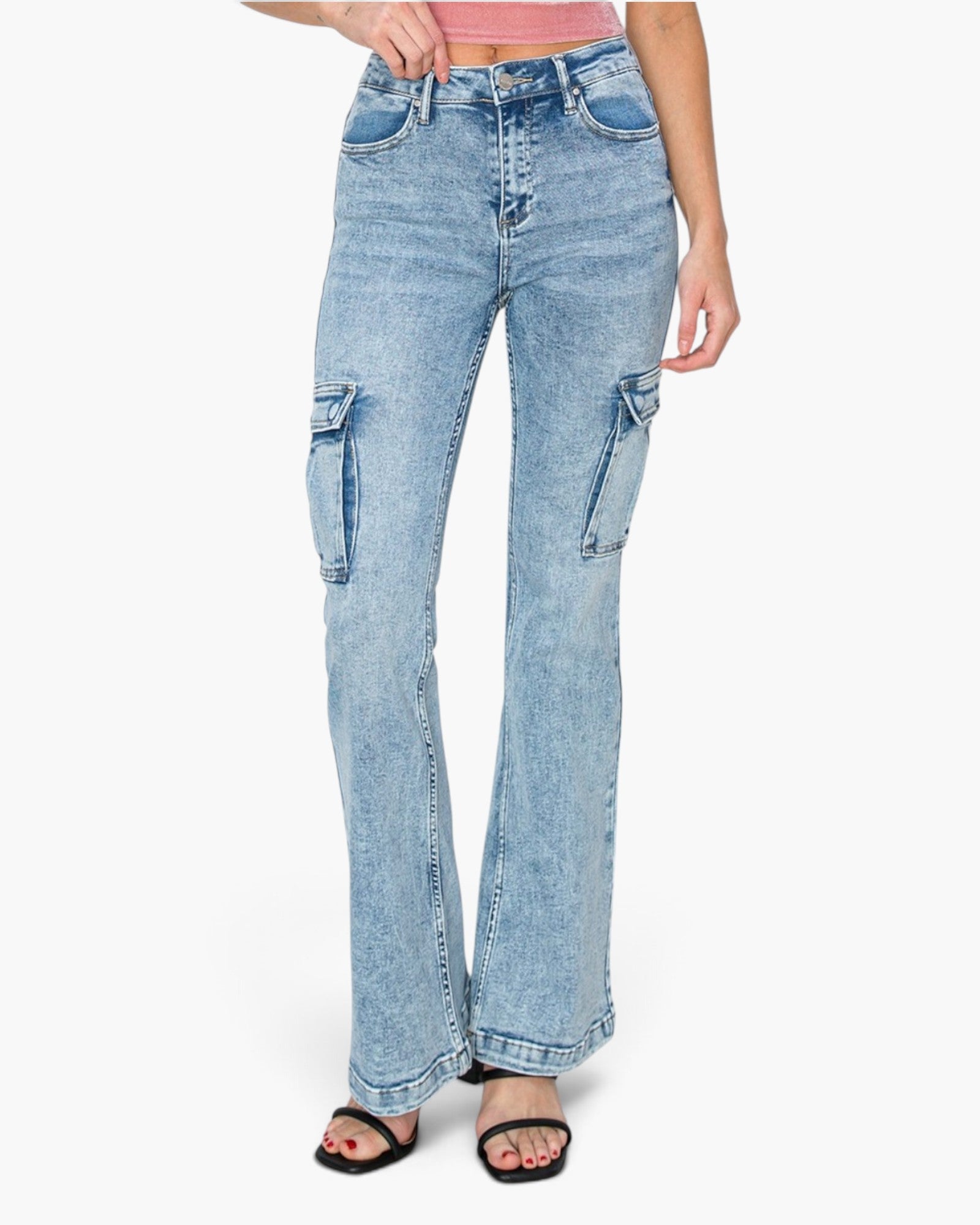 A model wearing light-wash blue denim cargo flare jeans, styled with a pink top and black slide sandals against a plain white background.