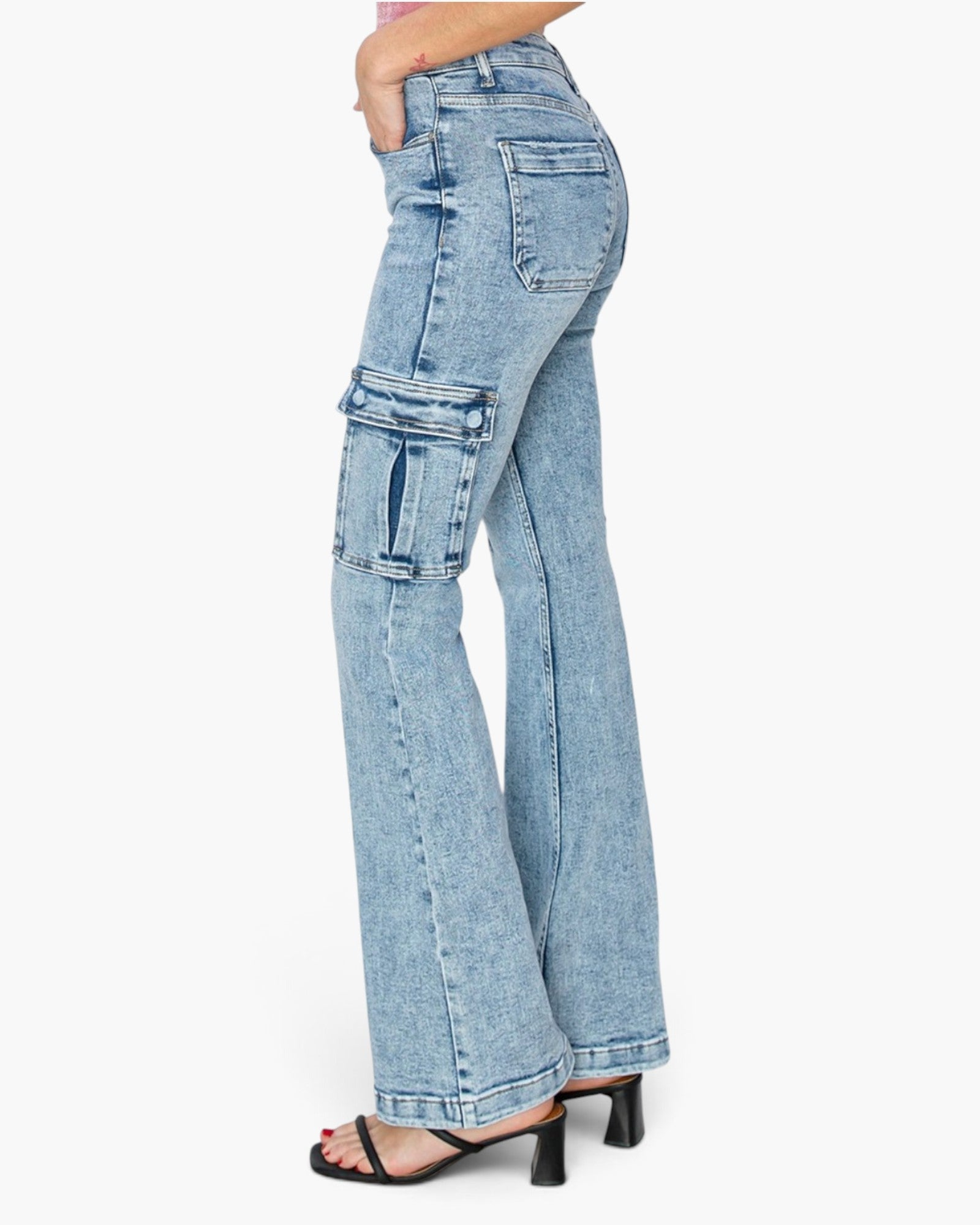 A side profile view of a model wearing high-waisted, light blue denim flare jeans with cargo pockets on the thighs, paired with black heeled sandals against a plain white background.