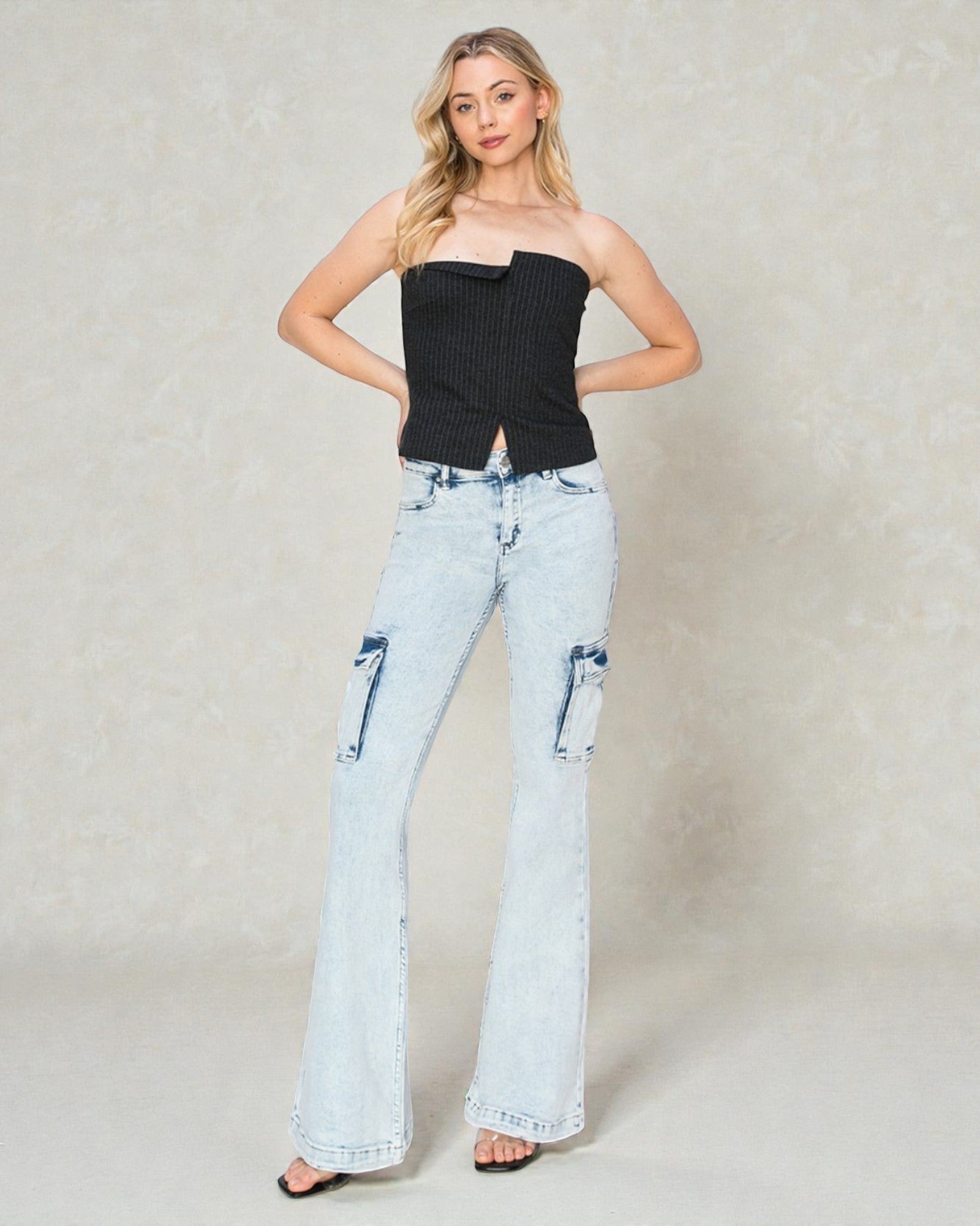 Woman wearing a black strapless top and light blue jeans on a plain background
