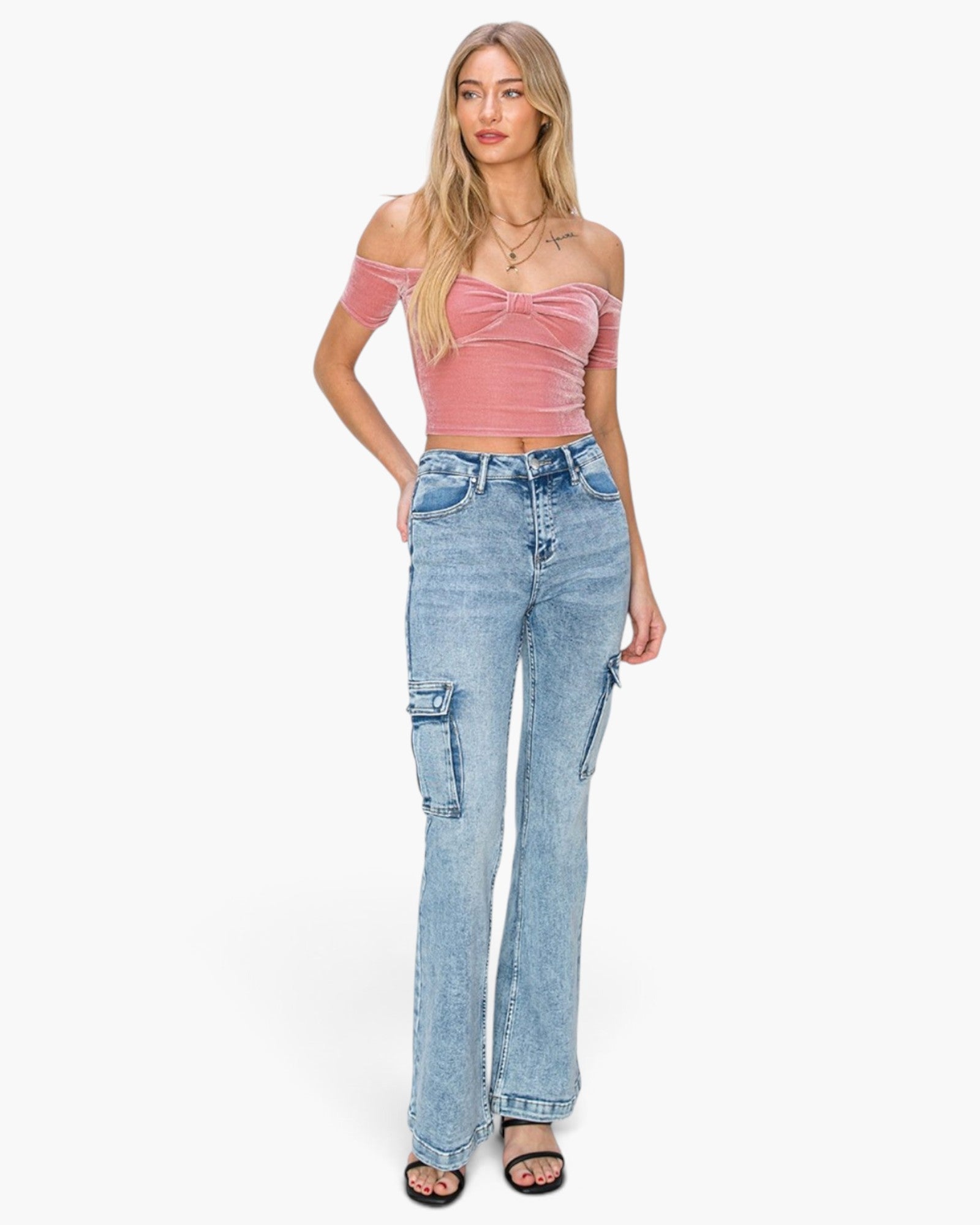 A woman modeling a pink off-the-shoulder crop top and light-wash blue high-rise cargo flare jeans against a plain white background.