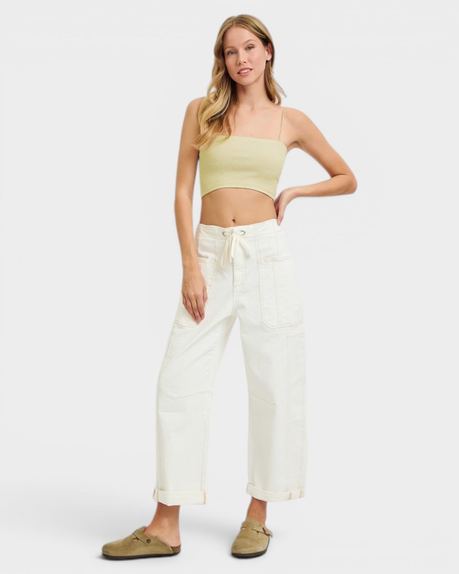 Woman wearing a light green crop top and white pants on a white background