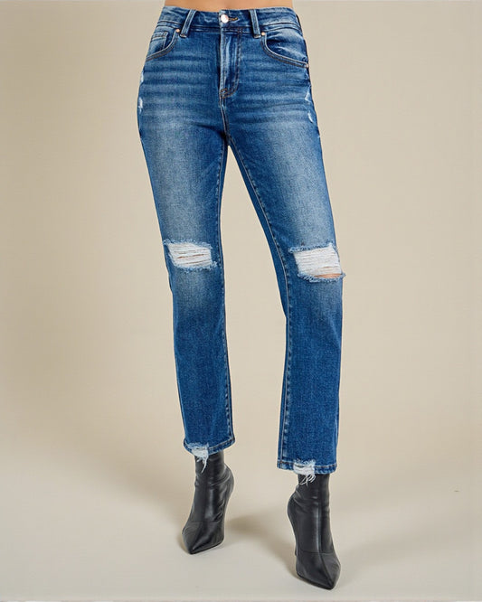 Blue jeans with distressed details worn by a person on a beige background