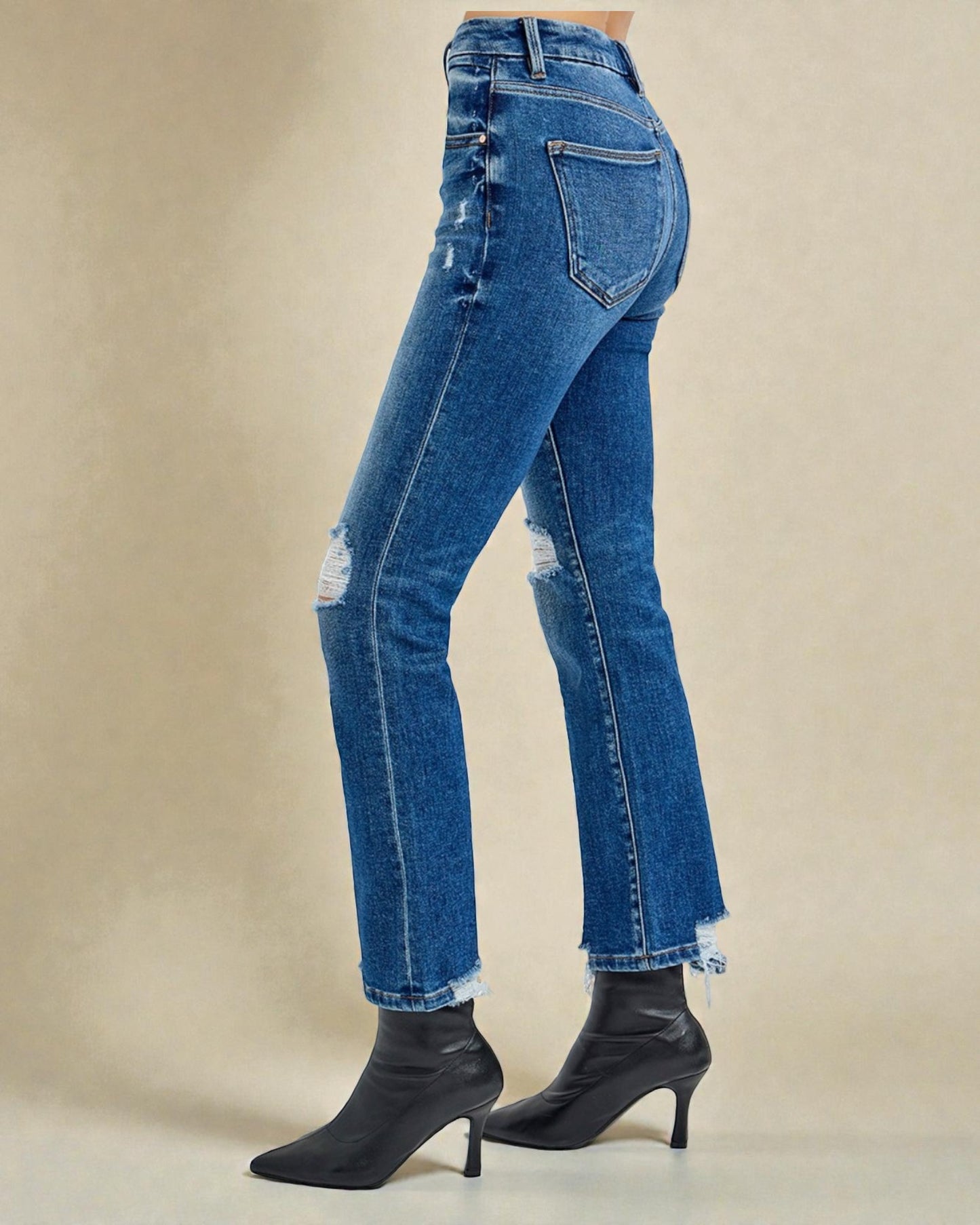 Blue jeans with a distressed look worn by a person on a beige background