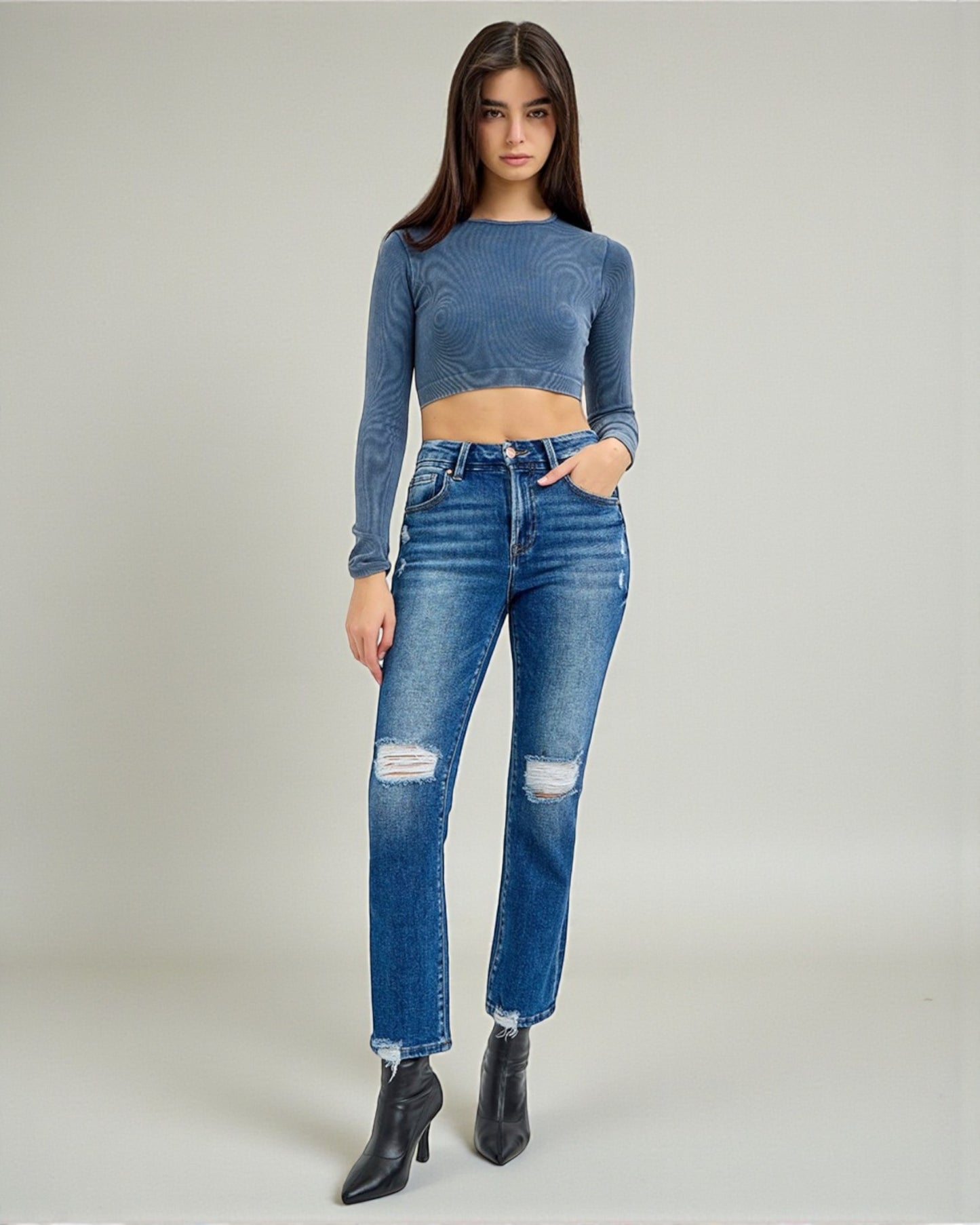 Woman wearing a blue long-sleeve top and distressed jeans on a plain background