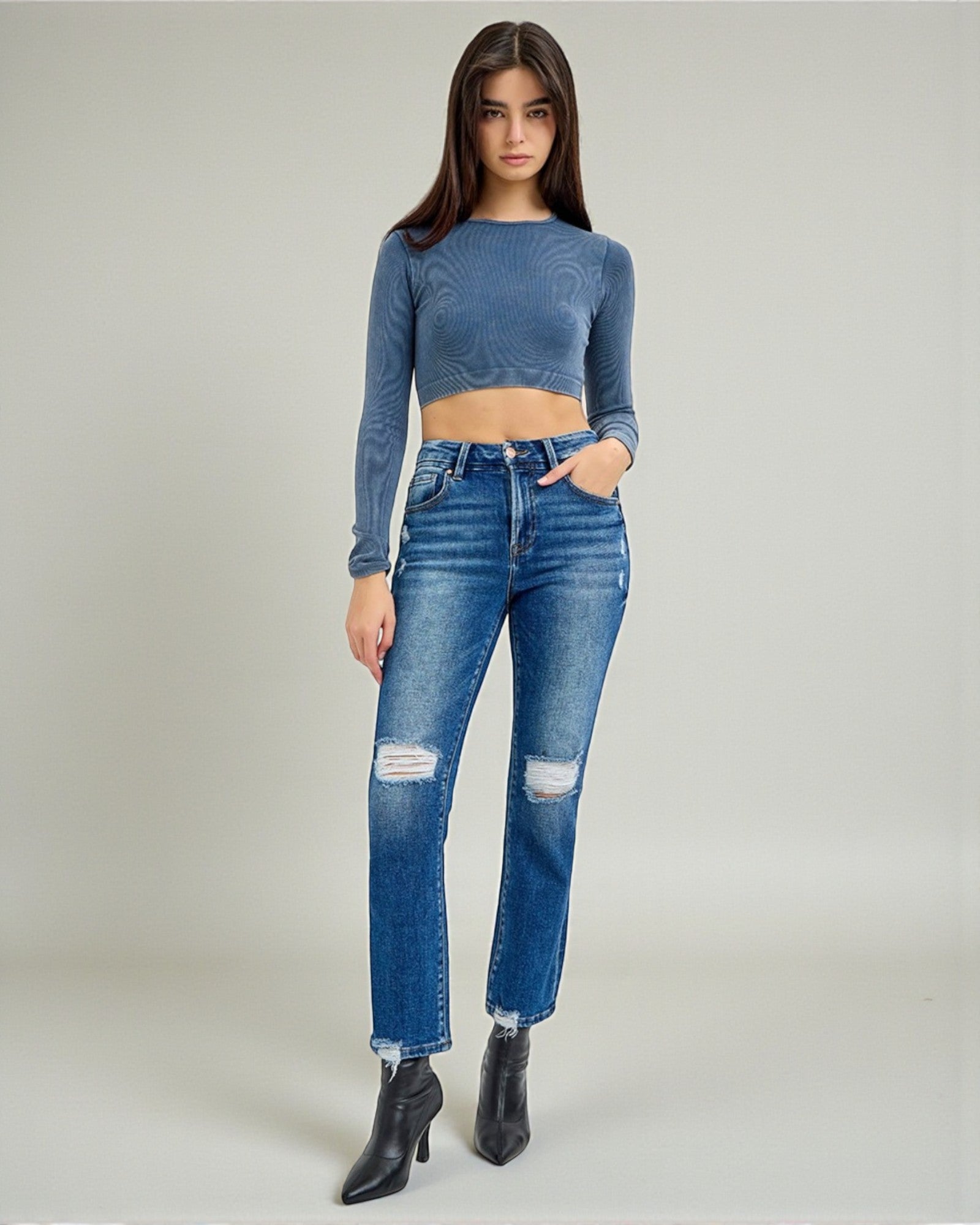 Woman wearing a blue long-sleeve top and distressed jeans on a plain background