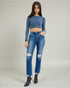 Woman wearing a blue long-sleeve top and distressed jeans on a plain background