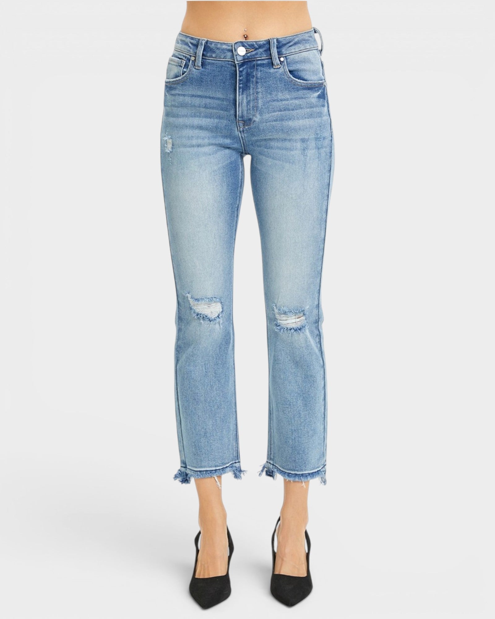 Light wash blue cropped jeans with distressed knee details and frayed hems, shown on a model wearing black pointed-toe heels against a light gray studio background.