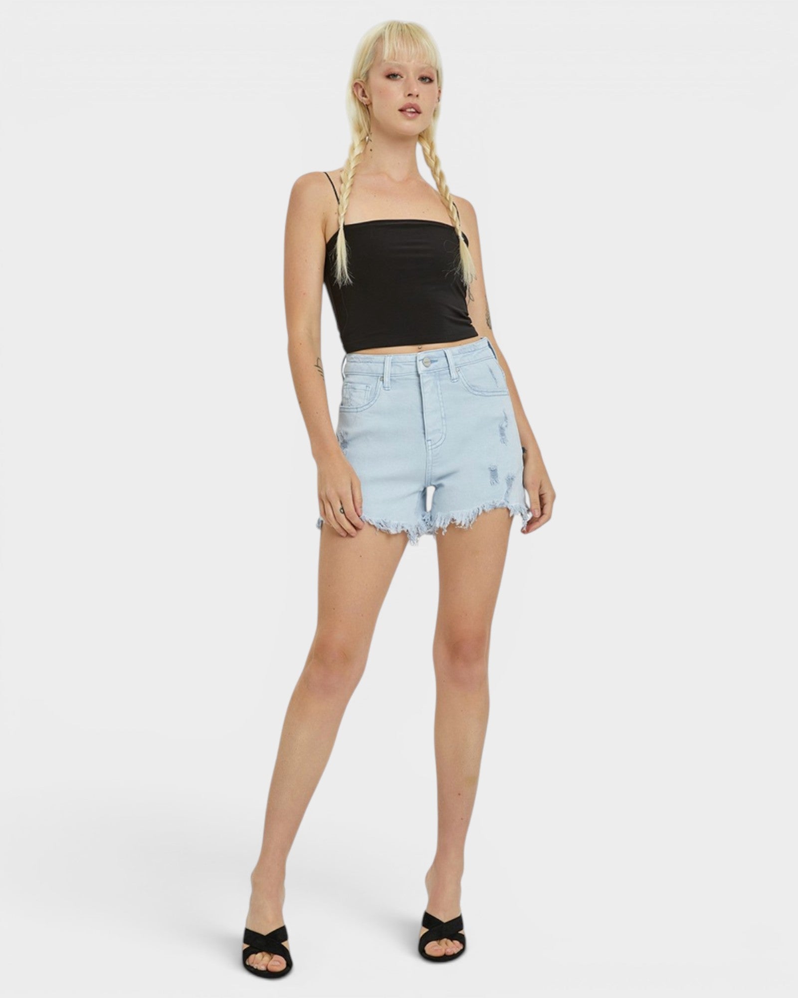 Woman wearing a black tank top and light blue denim shorts on a white background