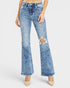 A model wearing a pair of light blue high-waisted flare jeans with a distressed rip on one leg, paired with beige pointed-toe heels against a light gray studio background.
