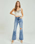 Woman wearing a white crop top with sequins and blue flared jeans on a light gray background