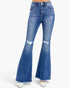 A pair of high-waisted, medium wash blue denim flare jeans with distressed details and frayed hems, shown on a model wearing white pointed-toe heels against a plain white background.