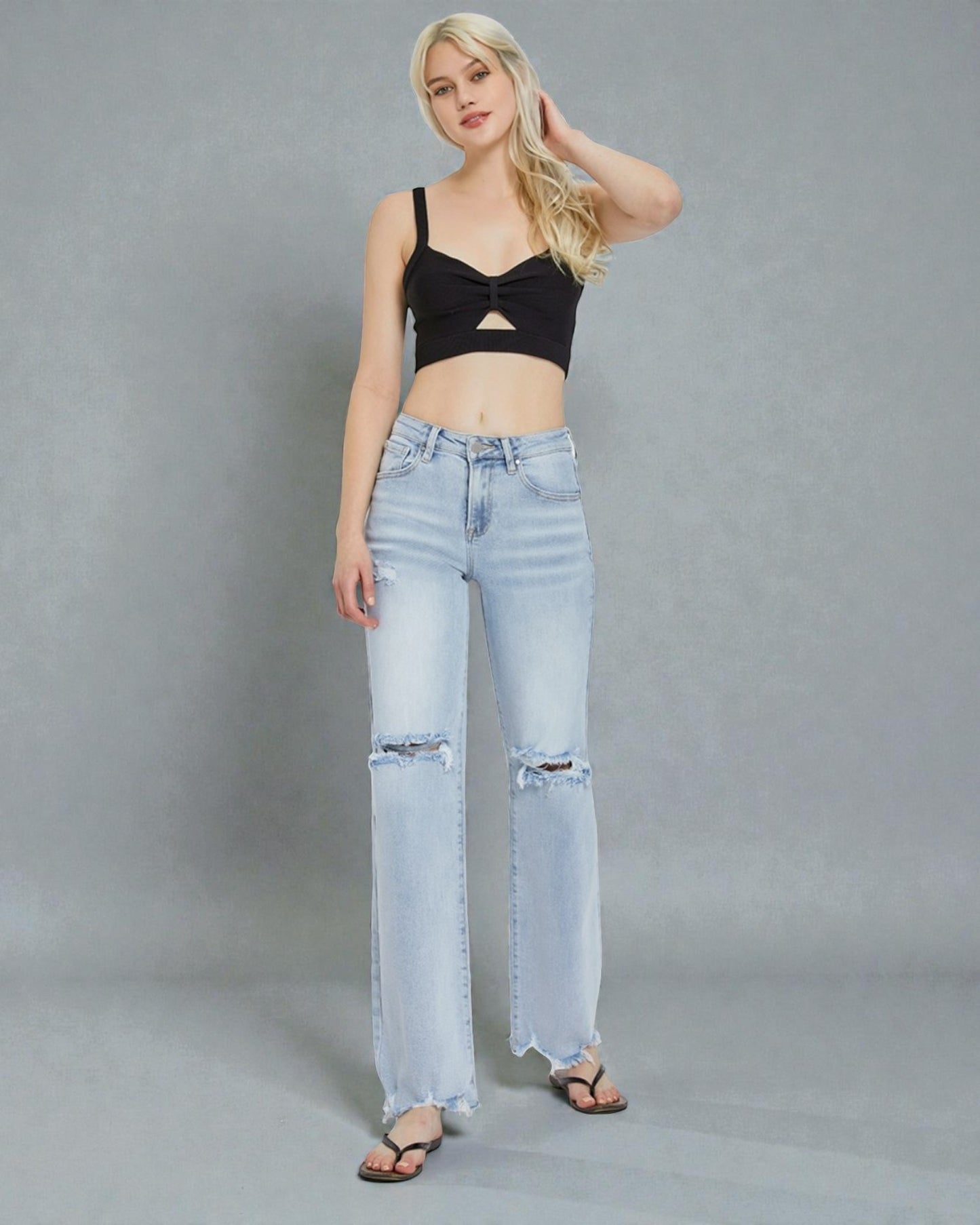 Woman wearing a black crop top and light blue jeans on a gray background
