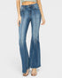 A model wearing a pair of medium-wash blue denim flare jeans with distinctive vertical seam detailing down the front of the legs, styled with clear-strap heeled sandals against a light gray studio background.