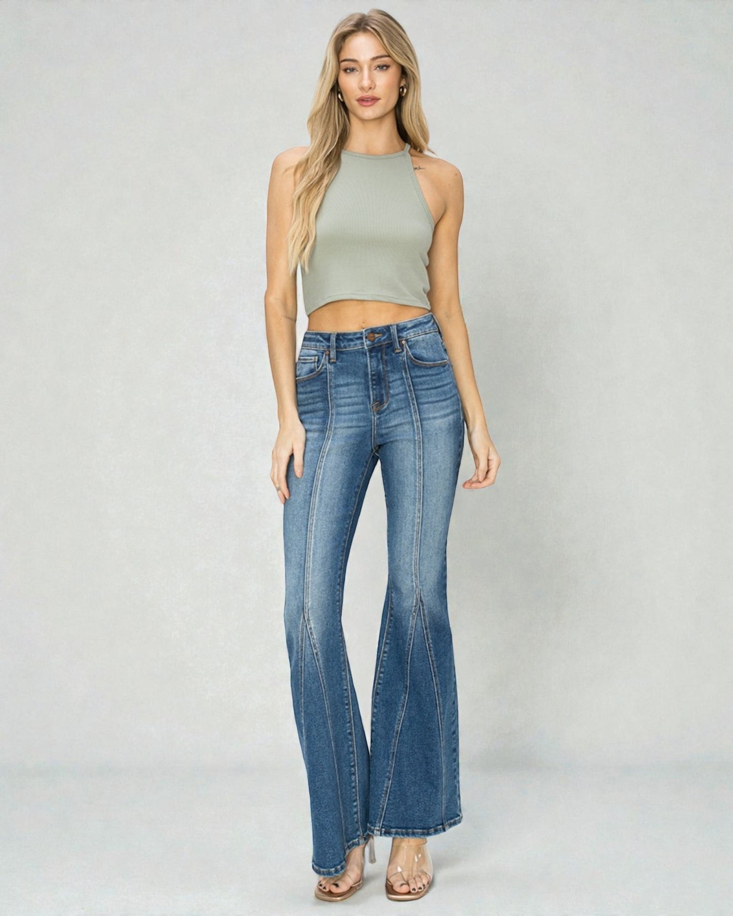 Woman wearing a green sleeveless top and blue flared jeans on a white background