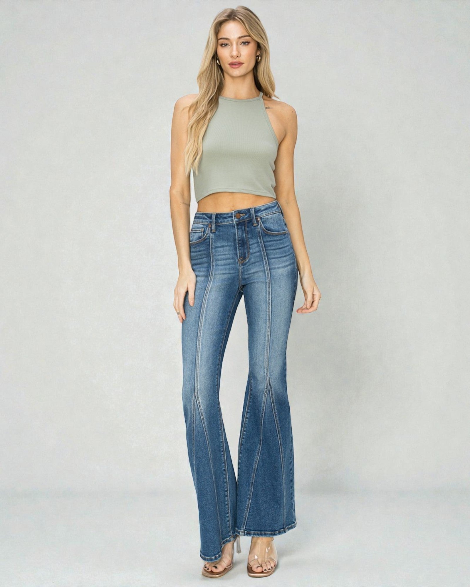 Woman wearing a green sleeveless top and blue flared jeans on a white background