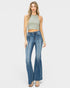 A woman modeling a sleeveless sage green crop top and blue high-waisted flare jeans against a light gray studio background.