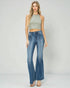 Woman wearing a green sleeveless top and blue flared jeans on a white background