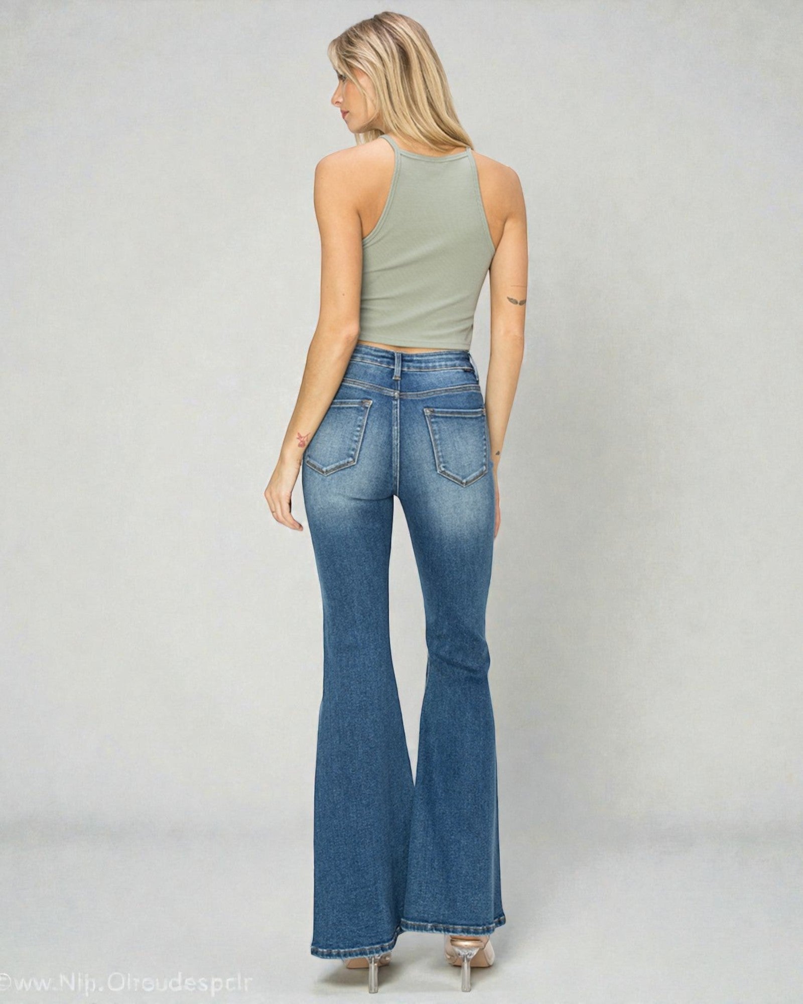 Woman wearing blue flared jeans and a green top on a plain background