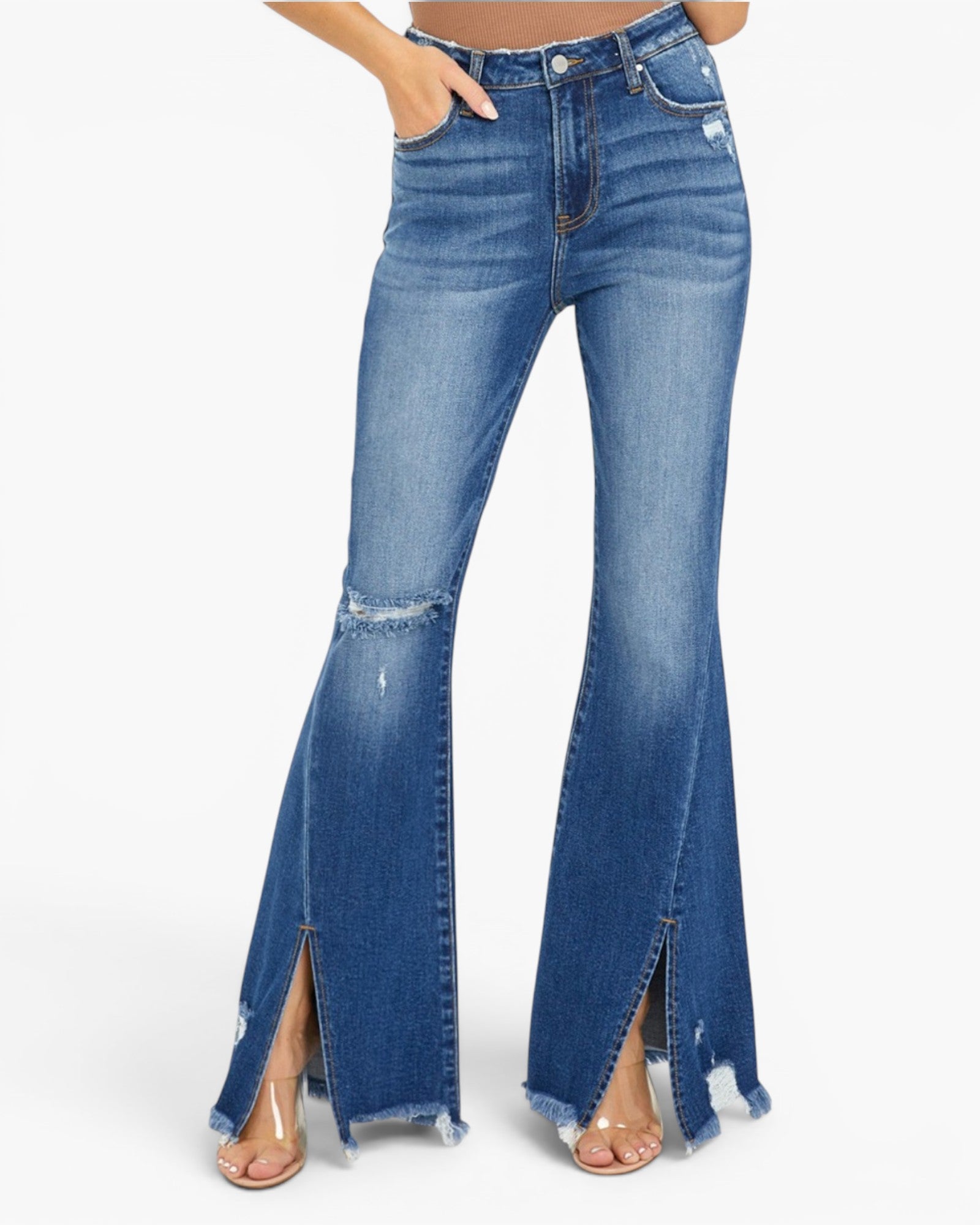 A model wears medium-wash blue denim flare jeans with distressed details and front slit hems, paired with clear high-heel sandals against a plain white background.